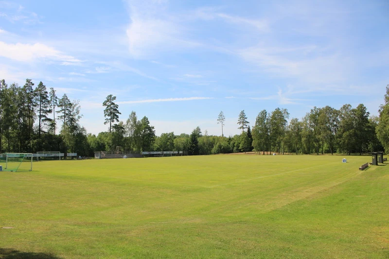 Bilden visar Linneryds idrottsplats omgiven av träd och grönska. Himlen är klar med några tunna moln.
