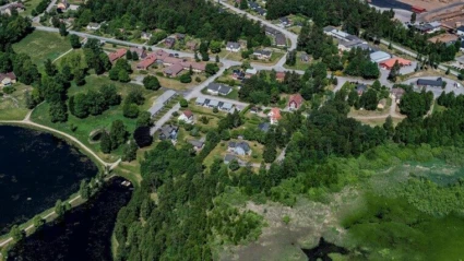 Flygbild över Linneryd med bostadshus omgivna av grönska. Till vänster syns en mörk sjö med en smal strandkant, och till höger ett område med tät vegetation och våtmark. Vägar slingrar sig genom bebyggelsen, och skogsområden omger husen i bakgrunden.