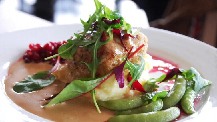En tallrik med en vällagad maträtt bestående av köttfärsbiff med gräddsås, potatismos, gröna sockerärtor, lingon och färska salladsblad som garnering.