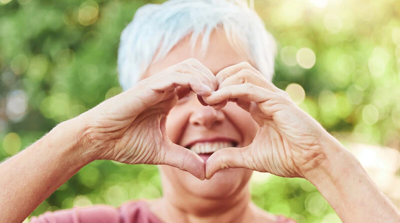 &Auml;ldre kvinna som formar sina h&auml;nder som ett hj&auml;rta framf&ouml;r sitt ansikte.