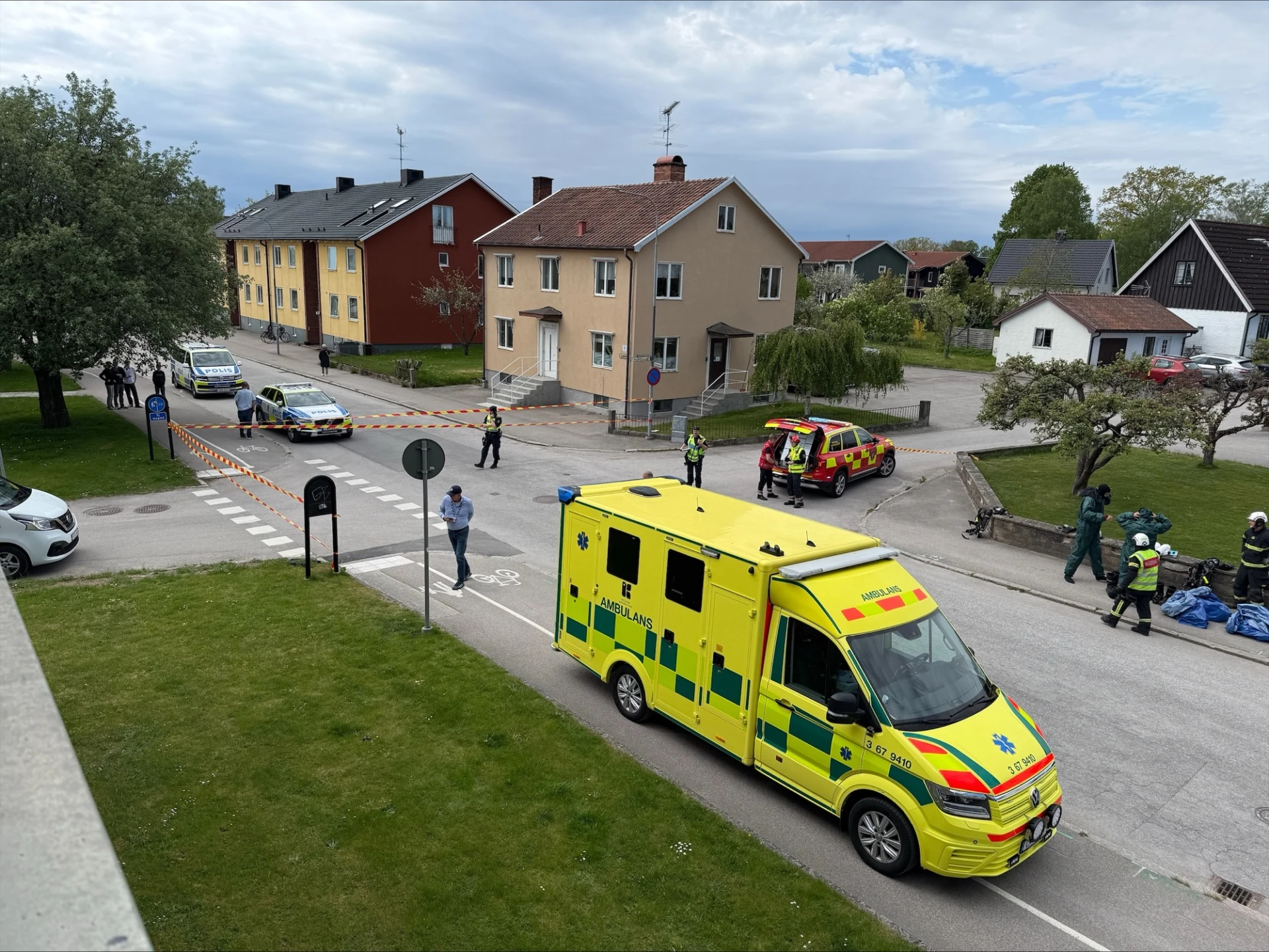 Ambulans, brandbil och polisbilar på avspärrad gata.