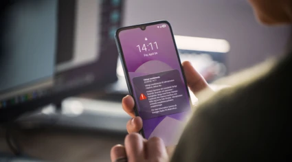 Person håller en mobiltelefon i handen inomhus och tittar på ett viktigt myndighetsmeddelande (VMA) på skärmen, med varning om en händelse i Malmö och uppmaning att stanna inomhus och följa information.