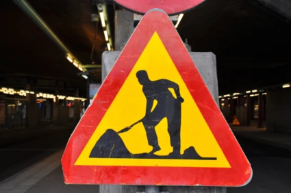 Skylt som visar byggarbetsplats, gul triangel med röd ram och svart tecknad gubbe som gräver.